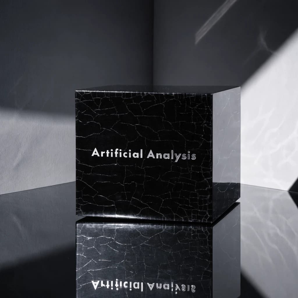 On the black box, silver foil embossing, centered: "Artificial Analysis" in Comic Sans Small Caps, perfectly justified. The letters are crisp, but the “Y” is duplicated faintly, ghosting right. On the box’s reflection, the word order is inverted: ARTIFICIAL ANALYSIS.