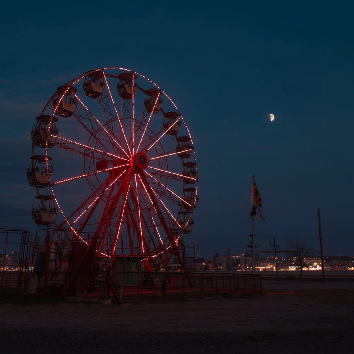 A deserted amusement park glows faintly under a half-moon. The ferris wheel is rusting yet strung with fresh, blinking LED lights. A torn clown banner flaps in a windless air. A lone balloon floats upward, tethered to nothing, while in the far distance city lights flicker on - some neon, some gas lamps as though from another century. 'Artificial Analysis' glows in neon