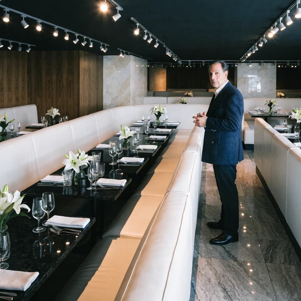 The place is almost empty. The banquettes are covered in white leather, the tables black granite, and the entire room is bathed in halogen track lighting that seems too bright. The maître d’ wears a double-breasted wool crepe jacket. There are lilies on every table.