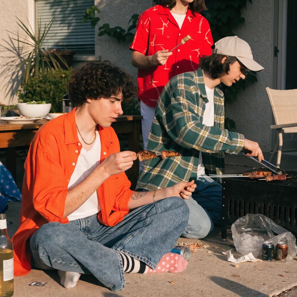 Friends grill skewers on a slightly messy patio.