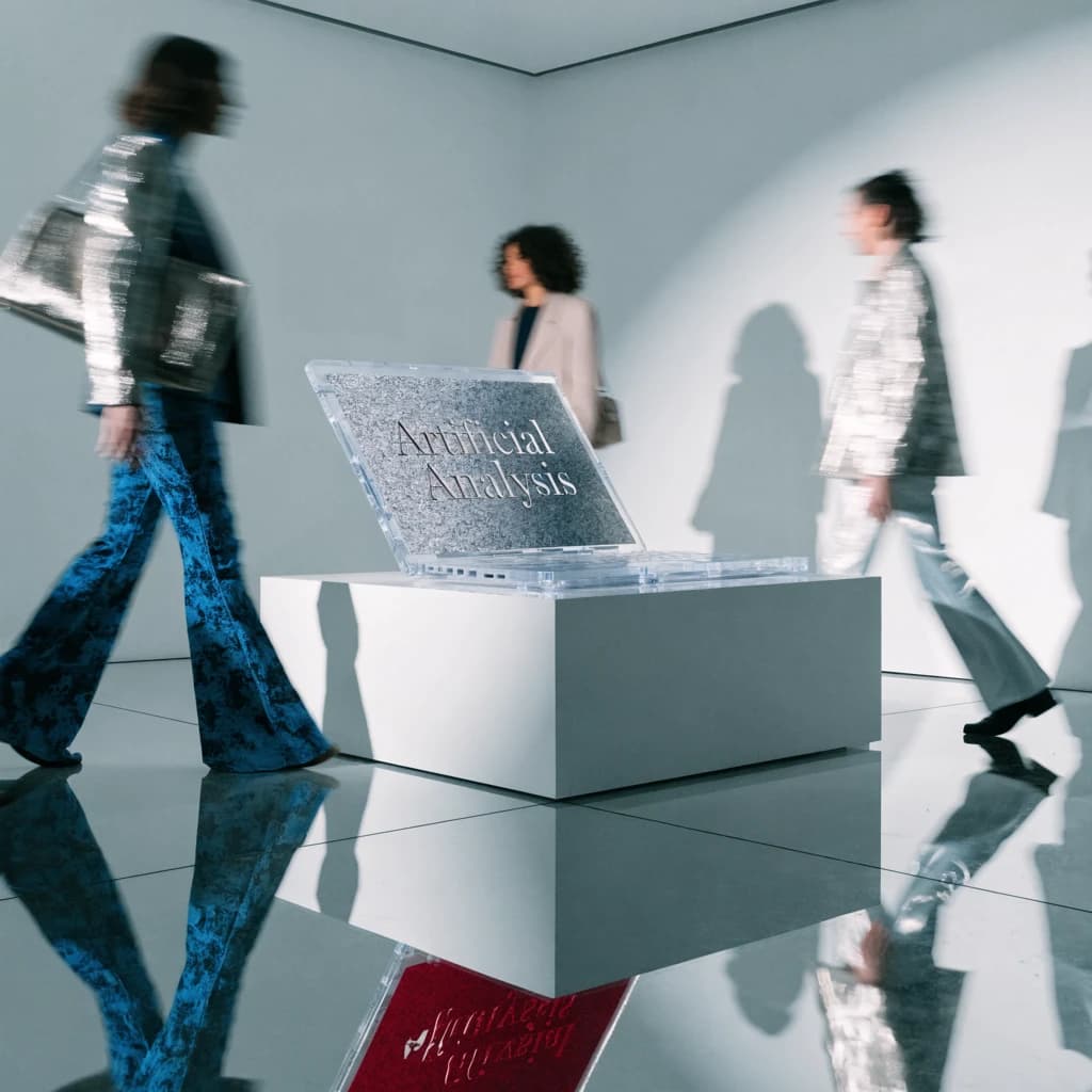In a spotless gallery space, a pedestal supports a transparent laptop whose screen flickers between static and pristine brand imagery. Shoppers blur past in designer clothes that appear slightly outdated - bell bottoms, metallic jackets. The embossed logo “Artificial Analysis” glints silver, yet its reflection in the glass floor reads in crimson letters. A single spotlight shines, though shadows fall in two directions.
