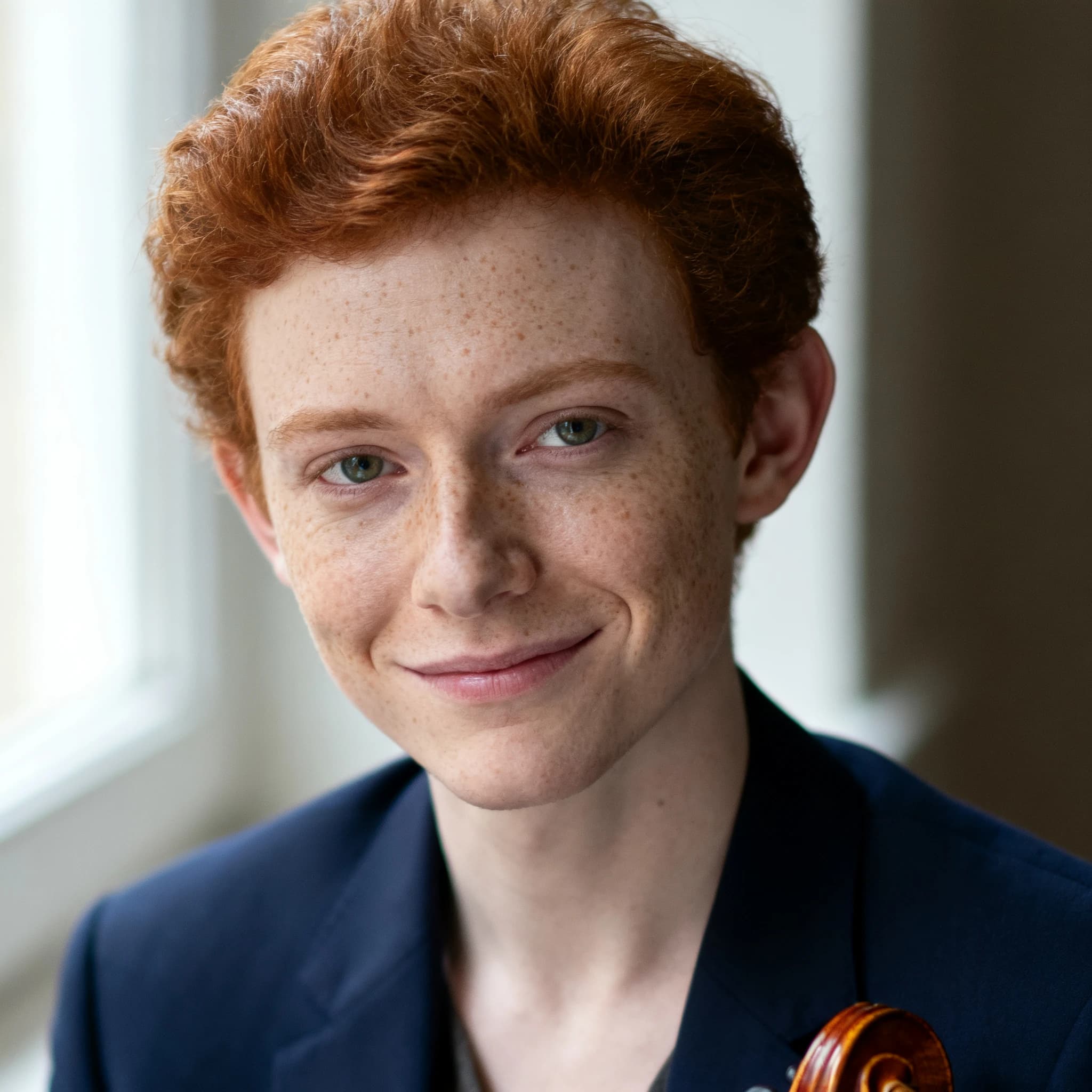 Capture a head-and-shoulders portrait of a freckled red-haired violinist in a navy blazer, soft window light, 85mm at f/1.8, gently smiling yet serious eyes, muted tones.