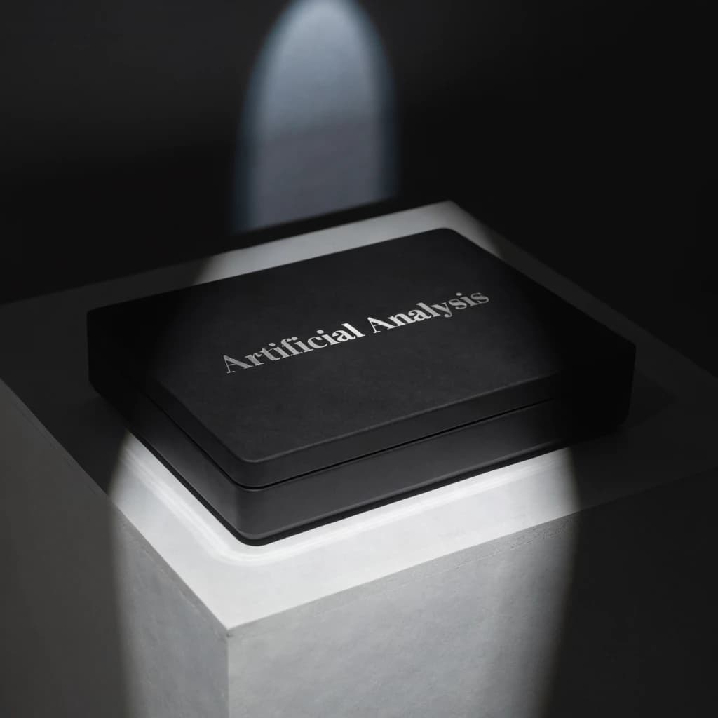 A premium matte black laptop-sized box rests on a pure white pedestal within a gallery space. Overhead, a single spotlight carves sharp contrast, leaving the edges in deep shadow. The brand name Artificial Analysis is embossed in silver foil, glinting faintly as though it were jewelry.