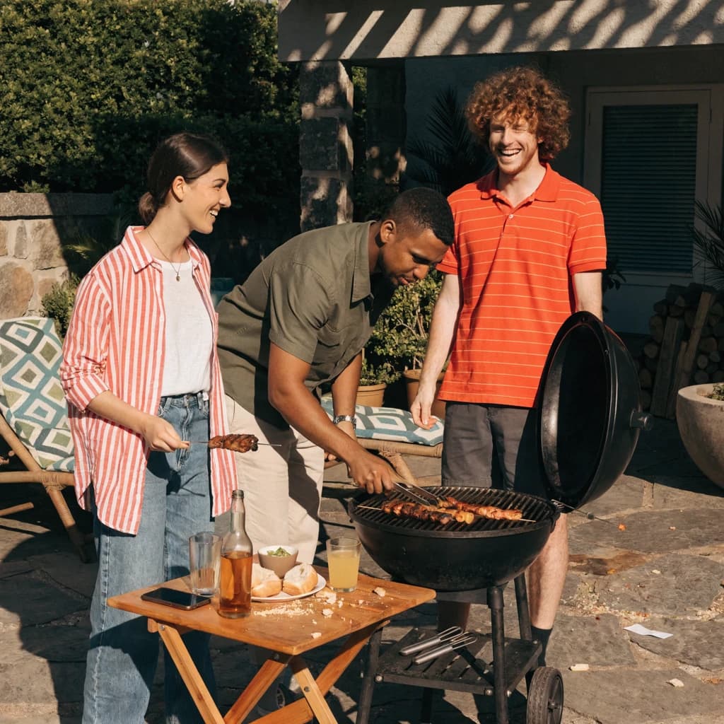 Friends grill skewers on a slightly messy patio.