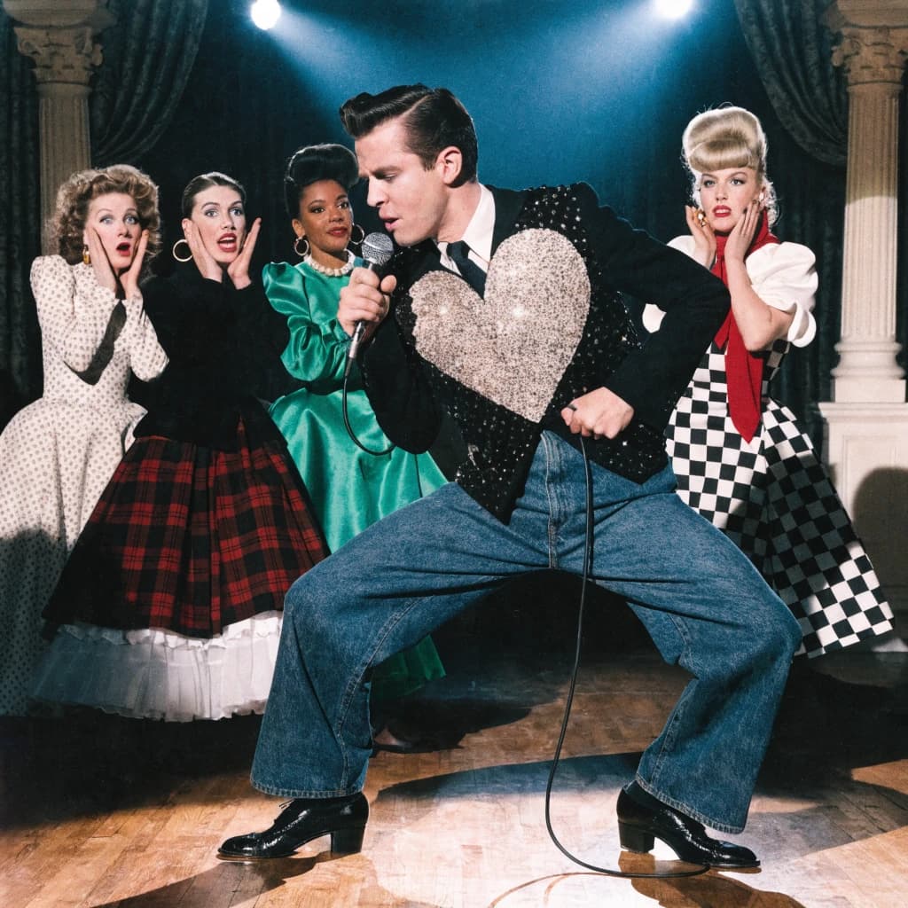 An archival image from 1953 of the rock singer swinging his hips on the stage while glamorous back up singers feign shock at his gyrations! He wears a diamond encrusted jacket with the stones arranged in the shape of a heart