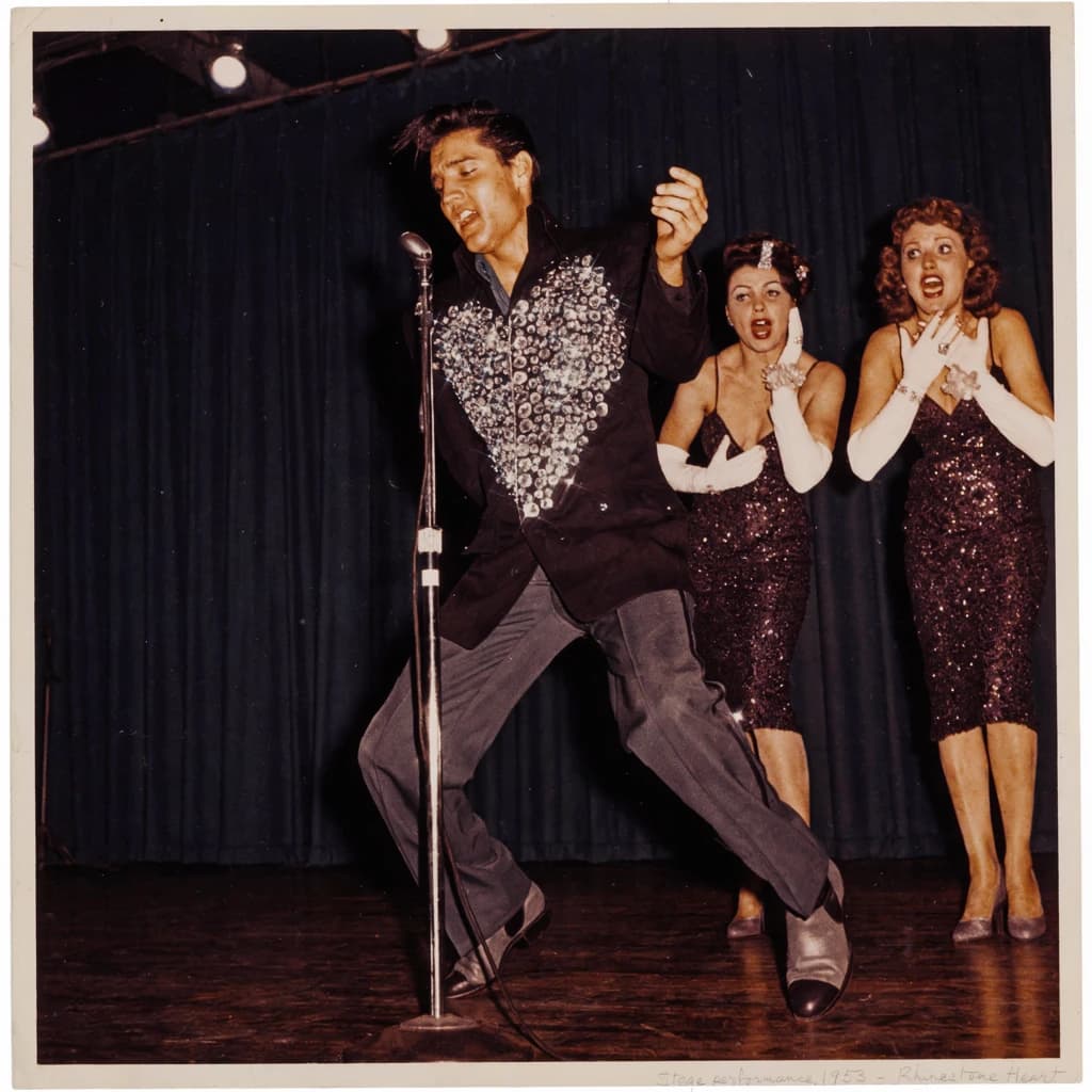 An archival image from 1953 of the rock singer swinging his hips on the stage while glamorous back up singers feign shock at his gyrations! He wears a diamond encrusted jacket with the stones arranged in the shape of a heart