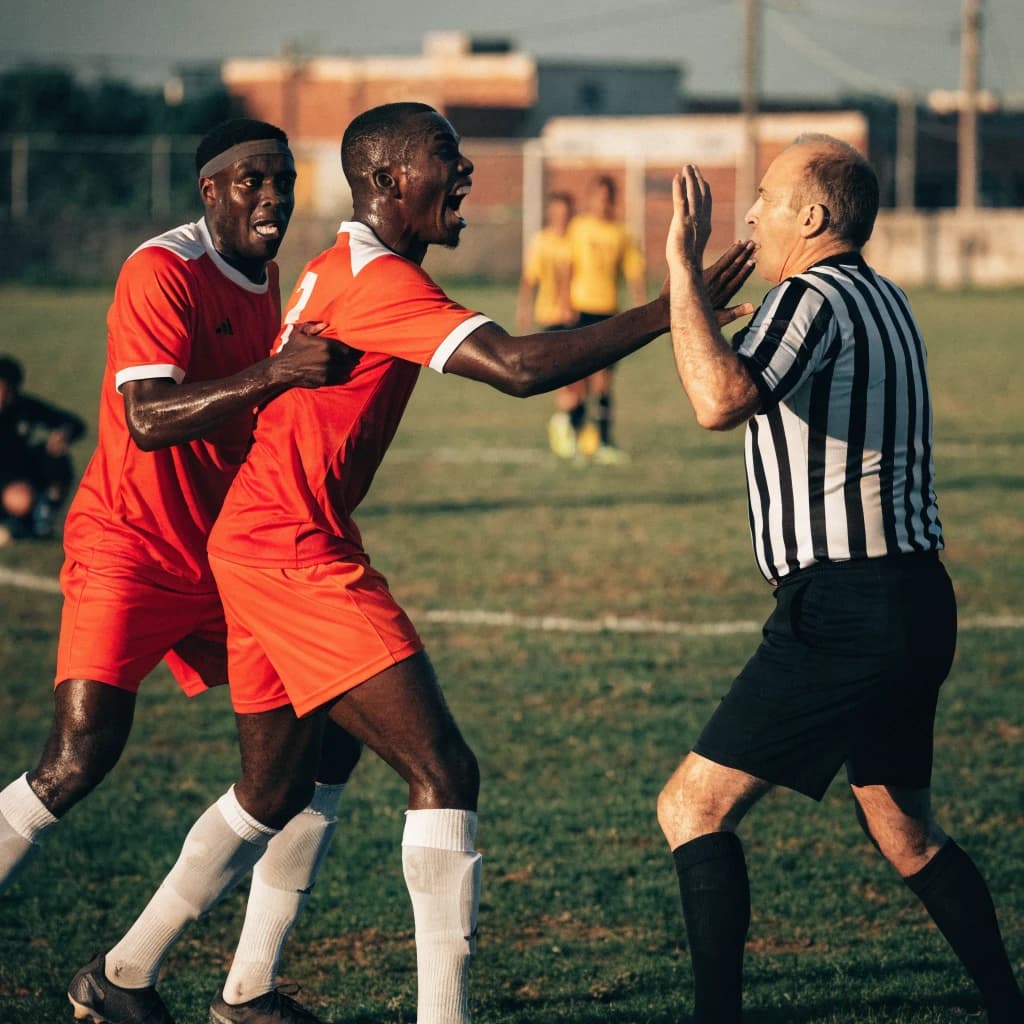 The soccer player clashes with the ref. It is thick and humid and the heat is getting to the players. His friend tries to pull him off before he causes any more trouble.