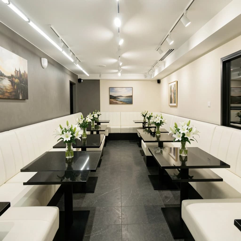 The place is almost empty. The banquettes are covered in white leather, the tables black granite, and the entire room is bathed in halogen track lighting that seems too bright. The maître d’ wears a double-breasted wool crepe jacket. There are lilies on every table.