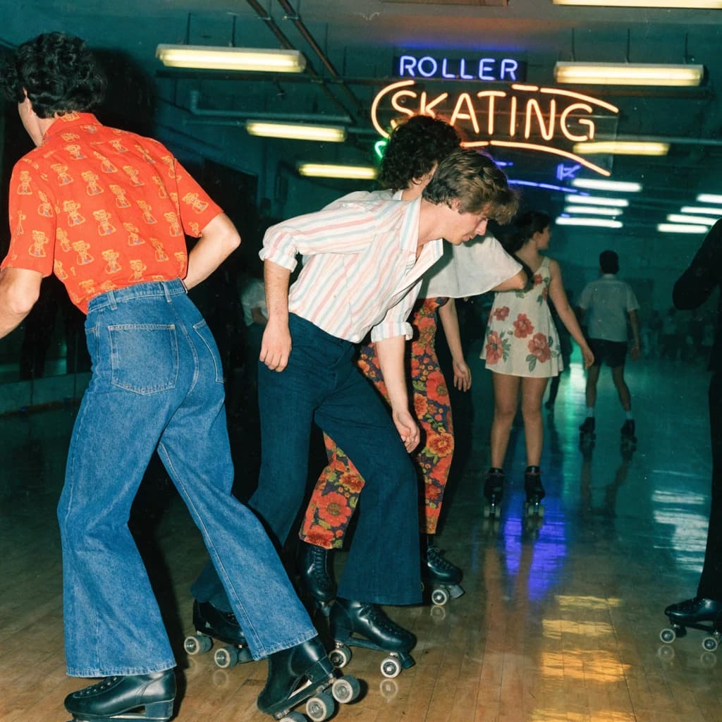 A 1970s roller rink crowd skates under neon, with a bit of fade and film grain.