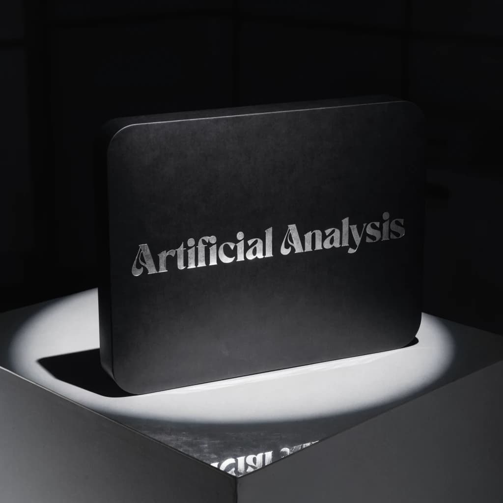 A premium matte black laptop-sized box rests on a pure white pedestal within a gallery space. Overhead, a single spotlight carves sharp contrast, leaving the edges in deep shadow. The brand name Artificial Analysis is embossed in silver foil, glinting faintly as though it were jewelry.