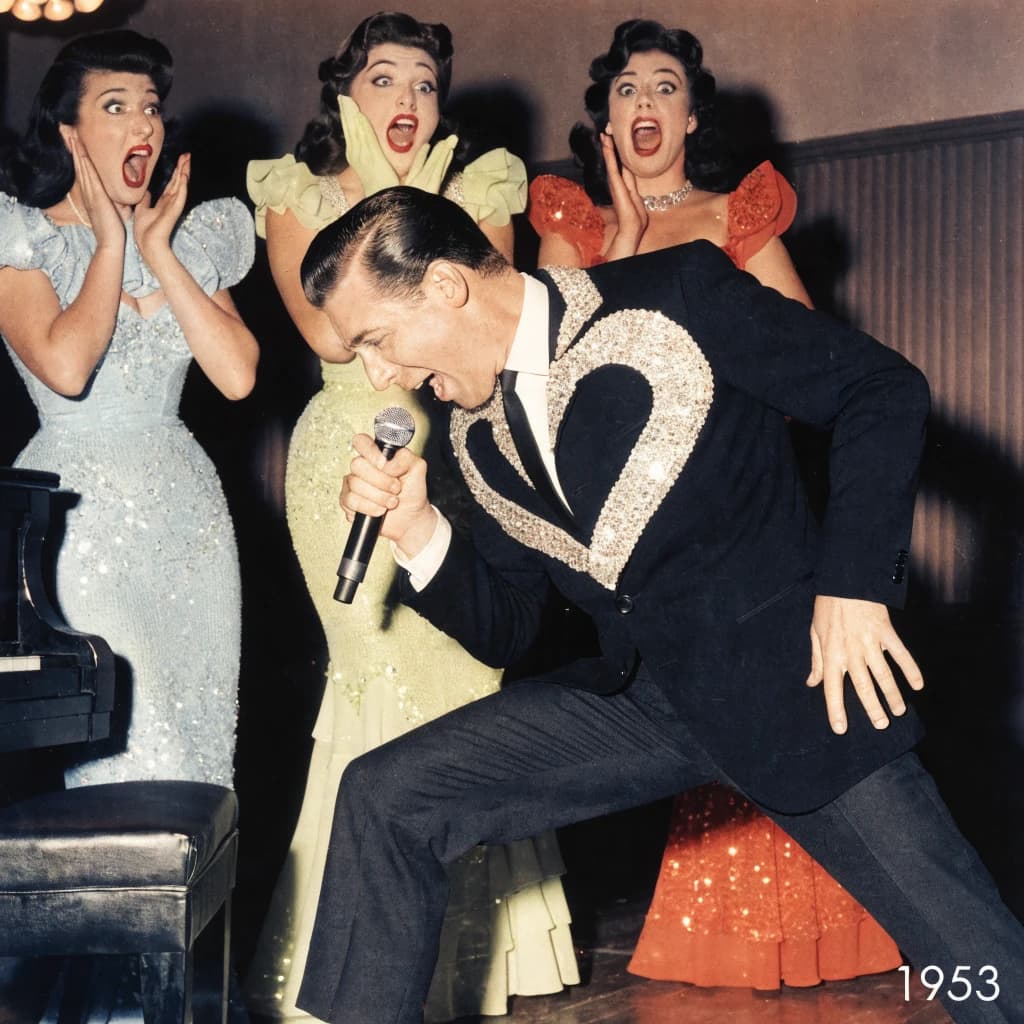 An archival image from 1953 of the rock singer swinging his hips on the stage while glamorous back up singers feign shock at his gyrations! He wears a diamond encrusted jacket with the stones arranged in the shape of a heart