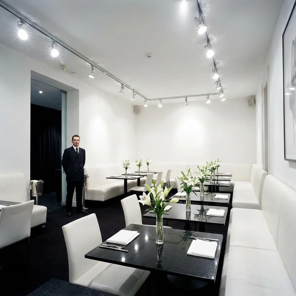 The place is almost empty. The banquettes are covered in white leather, the tables black granite, and the entire room is bathed in halogen track lighting that seems too bright. The maître d’ wears a double-breasted wool crepe jacket. There are lilies on every table.