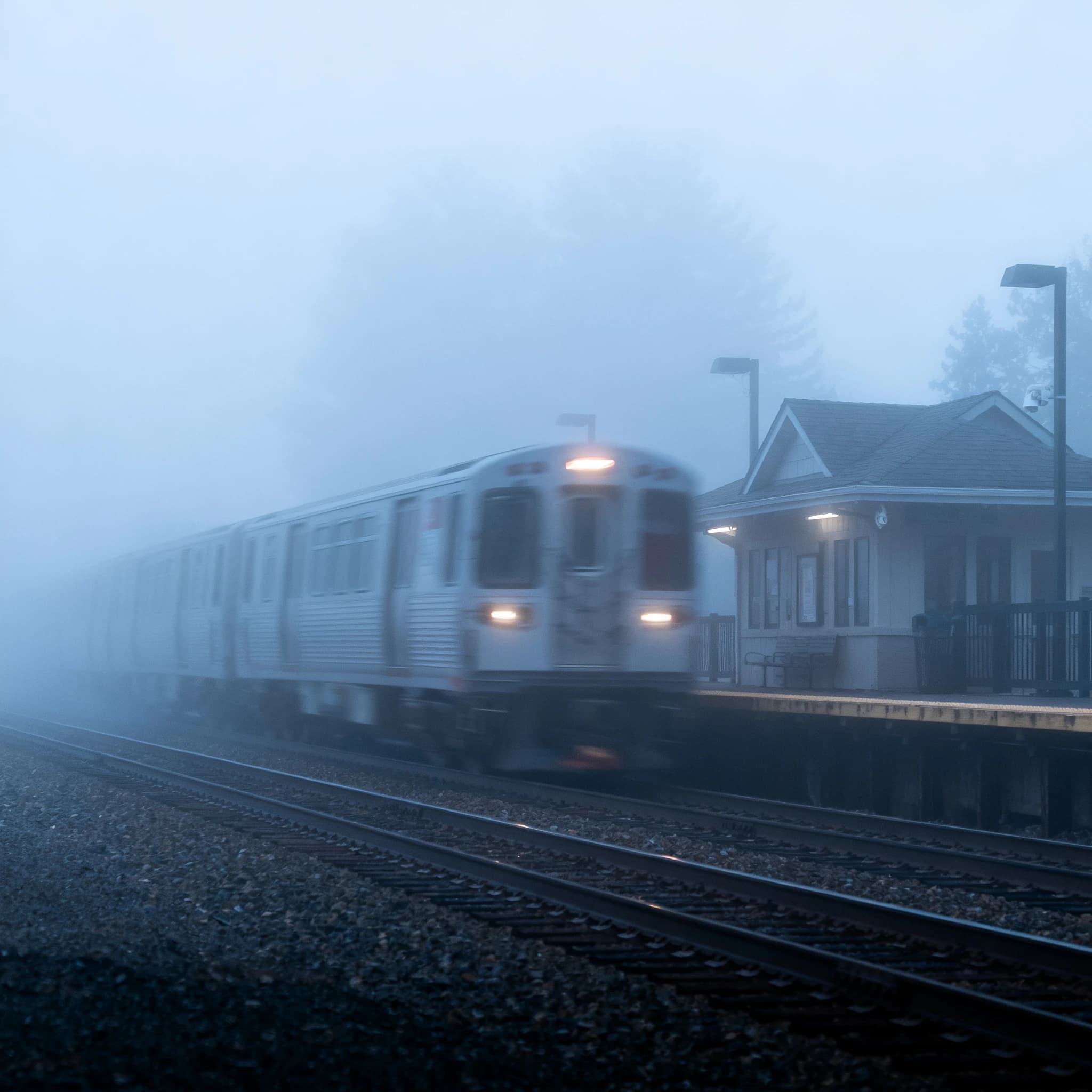 A commuter train enters a foggy little station.