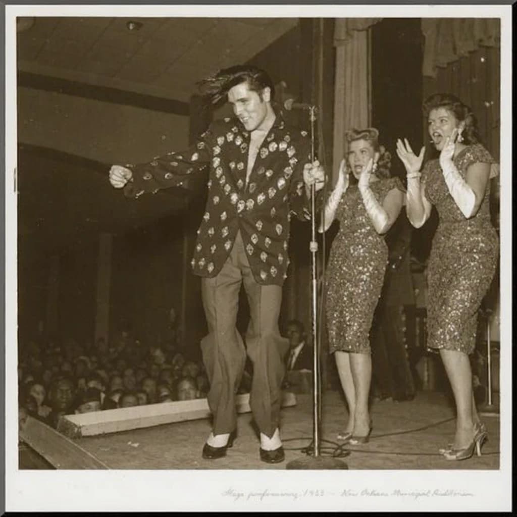 An archival image from 1953 of the rock singer swinging his hips on the stage while glamorous back up singers feign shock at his gyrations! He wears a diamond encrusted jacket with the stones arranged in the shape of a heart